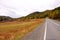 Straight asphalt road going through an autumnal valley at the slope of a high mountain range