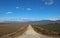 Straight country gravel road, in the plain and among the field, leading to the faraway mountains