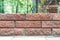 Straight lines of new fresh brickwork wall with blurred park or house backyard on background. Modern brick wall outdoors. Product