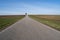 Straight rural road between farmland in the countryside with blue sunny sky in spring