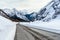 Straight stretch of a road running at the foot of towering snowy mountains