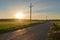Straight tarmac road on a green rice field landscape on a bright yellow sunrise landscape with electricity towers