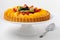Straight on view of a German fruit flan on a cake stand against a white background.