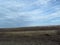 Stratocumulus grayish whitish clouds. Bare autumn fall winter grey brown field and blue sky. Countryside. Gloomy weather.