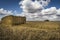 Straw bale, tractor on the horizon, fluffy cloud blue skies