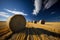 Straw bales in a field under a blue sky with clouds