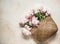 Straw basket bag with a bouquet of peonies on a light concrete background, top view