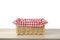 Straw basket decorated red checked picnic cloth on wooden background isolated