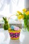Straw bright basket with colored easter eggs, bouquet of yellow tulips and daffodils flowers and green bunny rabbit on