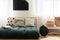 Straw handbags next to stylish black vase and fancy sofa with pillows made of futon, black poster on the wall between windows