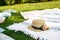 Straw hat with fresh flowers lay on a white picnic blanket at green lawn bright summer day background. Summer weekends