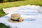 Straw hat with fresh flowers lay on a white picnic blanket at green lawn bright summer day background. Summer weekends leisure