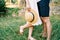 Straw hat in the hand of woman standing next to man in the garden. Cropped. Faceless