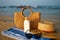 Straw hat rests next to sunscreen bottle on blue towel sunglasses, beach bag on sandy shore. Summer essentials for skin