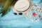 Straw hat, sunglasses, palm leaves, rope, seashell and starfish on turquoise table top view. Summer holidays, travel and vacation.