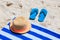 Straw hat, towel and flip flops on a sand beach