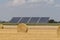 Straw roll bales with crop field, photovoltaic panel and blue sky in background