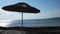 A straw umbrella on a beautiful pebble beach. Concept. Summer straw umbrella and the reflection of the sun in rippled