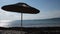 A straw umbrella on a beautiful pebble beach. Concept. Summer straw umbrella and the reflection of the sun in rippled