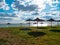 Straw umbrellas on green grass harsh shadow, sand beach vivid blue sea water sky background sunbeam. Scenic landscape