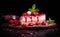 Strawberry cheesecake slice with red sauce topping and fresh strawberries, on a wooden platter against a dark background