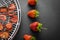 Strawberry chips on a round white plastic lattice for drying fruits next to four ripe strawberries on a dark background