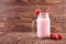 A strawberry shake in a mason jar. Pink berry drink on a wooden background. A yogurt with a strawberry on top and a red straw.