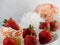 Strawberry shortcake cupcake sitting on a white plate with fresh strawberries and more berries and a pink and white flower in the