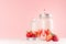Strawberry smoothie in retro glass jar with bright sliced berries, straw and silver lid on light, soft, pink background.