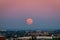 The strawberry Supermoon at sunset gradient from blue to pink on the city skyline in June 2020 in Spain