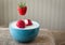 Strawberry suspended over a blue glass bowl of milk and strawberries.
