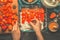 Strawberry tiramisu cake making. Womans female hands laid strawberries on the cake on dark rustic wooden background, top view.