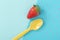 Strawberry with yellow spoon on two tone blue background