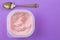 Strawberry yogurt in plastic cup isolated on lilac background - Top view photo of pink yoghurt and small silver spoon - text space