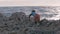 Stray boy throws stones on the seashore. Caucasian child in dirty clothes playing on the beach against the stormy sea background.