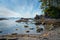 Streaky clouds block out the blue sky over the rocks, beach and ocean water of Botanical Beach, BC