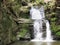 A stream with a big waterfall on a rock with green vegetation in the natural protected landscape area of the ReÅ¡ov waterfalls