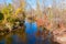 Stream lined with converging autumn color trees reflected disappears into distance