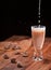 A stream of milk is poured into a glass with a milk drink with a splash of drops. Chocolate candies lie on a wooden table