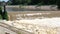 Stream of muddy water flowing rapidly passing a small dam.