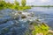 Stream with rapids along the grassy green edge of a lake below a blue sky in summer