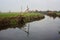 Stream of water in the countryside and a mooring pole by the shore with its reflection casted in the water on a cloudy day