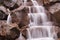 Streams of water flowing down huge boulders. Stone waterfall