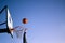 Street basketball ball player throwing ball into the hoop. Close up of hand, orange ball above the hoop net with blue sky in the