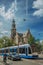 Street with blue sky, old church, people, cyclist and tram passing by in Amsterdam.
