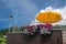 Street cafe summer terrace fragment: yellow parasol and beautiful flowers against the blue sky