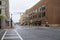 A street with cars driving surrounded by red brick buildings with Dillards, tower cranes, black light posts and signs