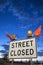 Street closed` roadsign with orange flags on it under a cloudy sky in the evening`