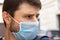 Street closeup portrait of a frowning caucasian man in protective blue medical mask in period of pandemic coronavirus covid-19