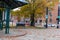 A street corner covered with fallen autumn leaves with a green pergola and a green park bench surrounded by gorgeous autumn trees